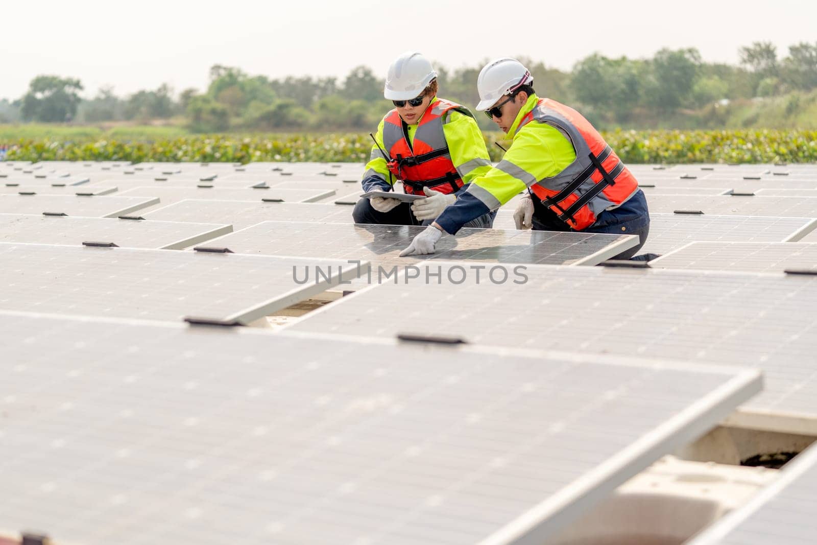 Two professional technician workers sit and work together and work with solar cell panel on base over water reservoir.