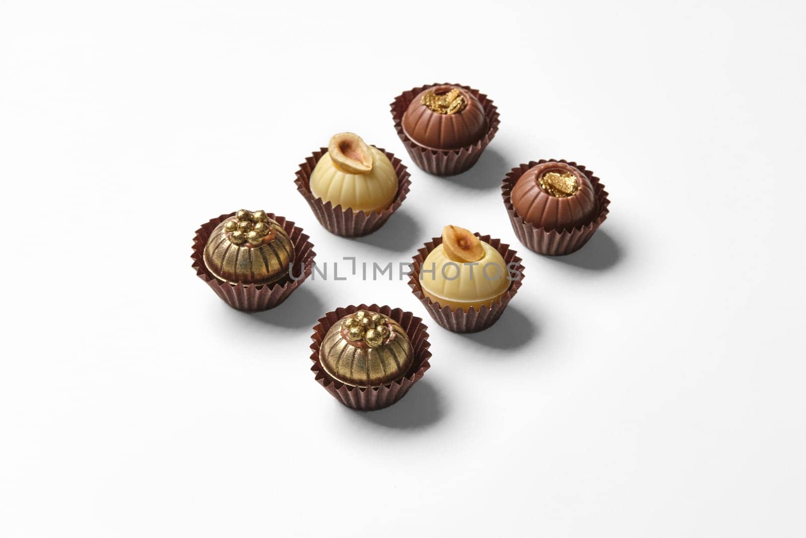 Elegant artisan chocolates decorated with hazelnuts, caramel crumbs and golden pearls, on white background