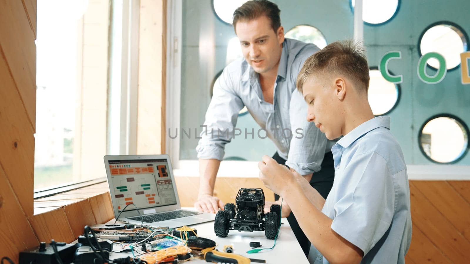 Caucasian teacher help student fixing car model and giving advise for programing system or coding prompt while highschool boy listen and use equipment to repair robot at STEM classroom. Edification.