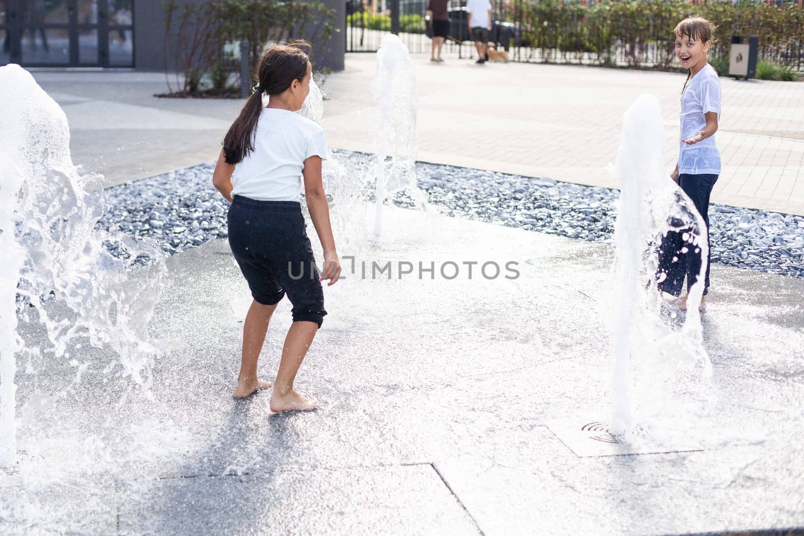 Happy teenage girl dancing in a fountain in a city park on a hot summer day. High quality photo