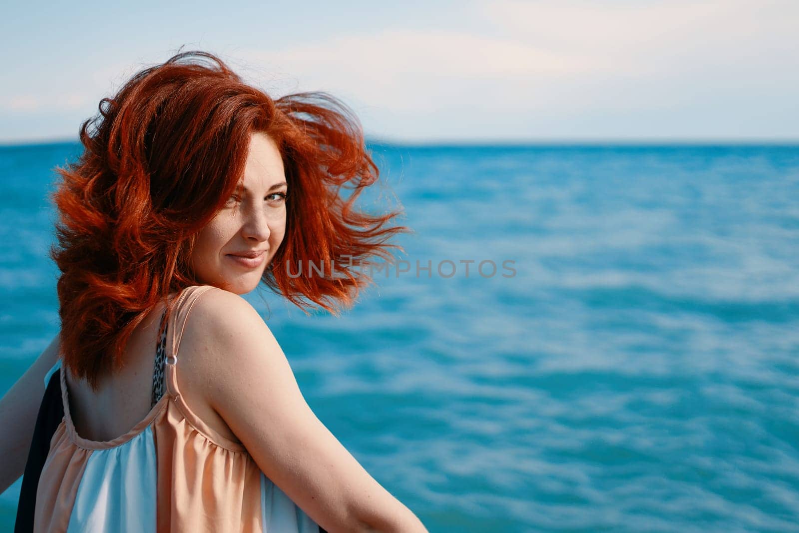 A beachside portrait capturing a young woman glancing over her shoulder with the azure sea as the backdrop.