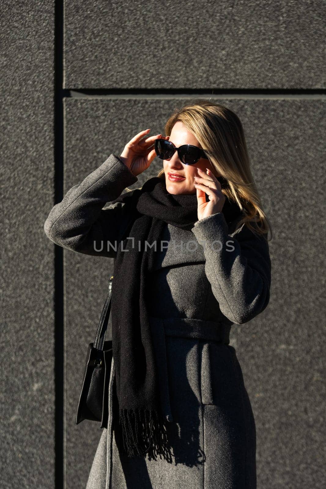 Beautiful young stylish blonde woman wearing long coat walking through the city streets. Trendy casual outfit. Street fashion. . High quality photo
