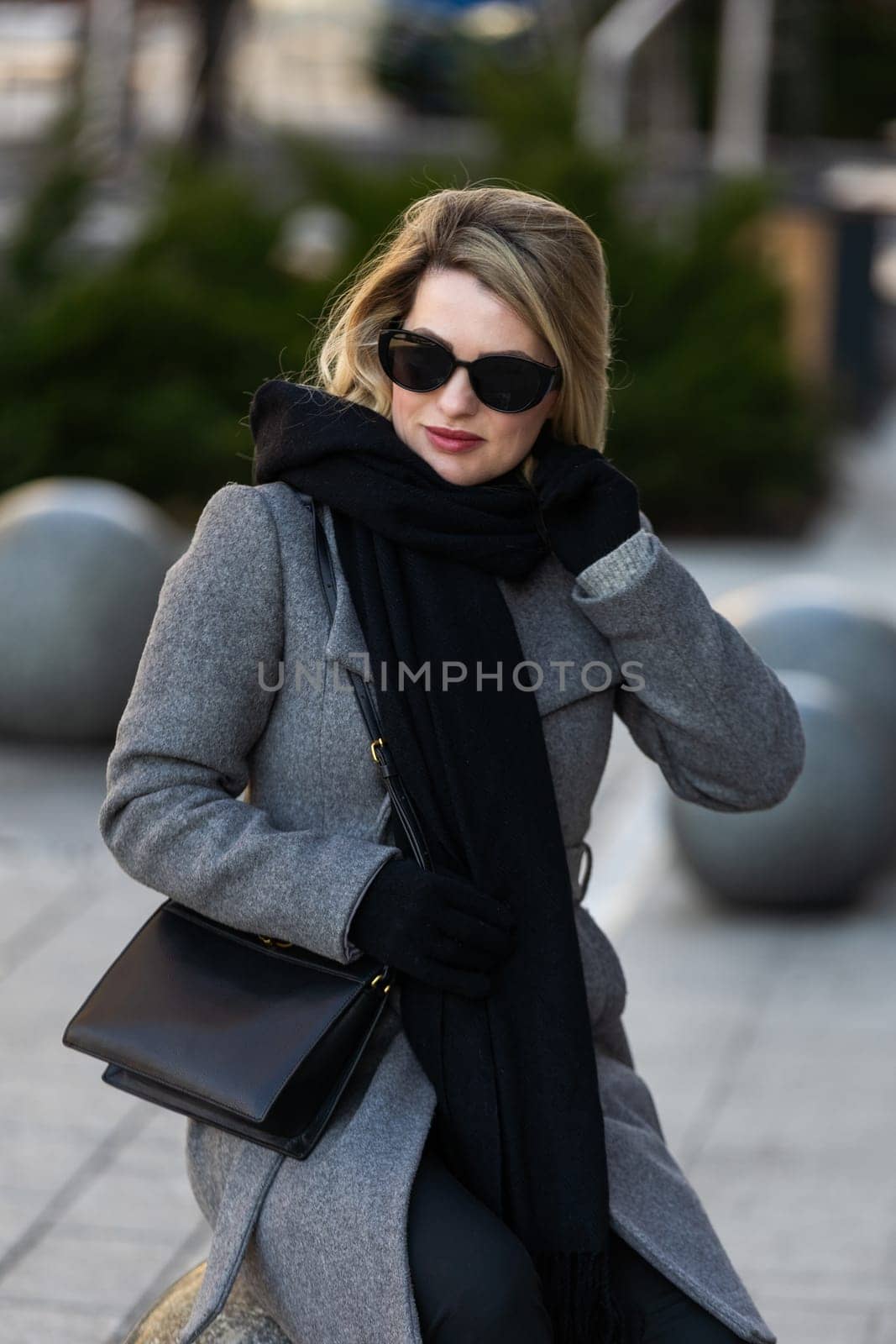 Young beautiful blonde girl in coat with a black bag walks through the winter and spring city by Andelov13