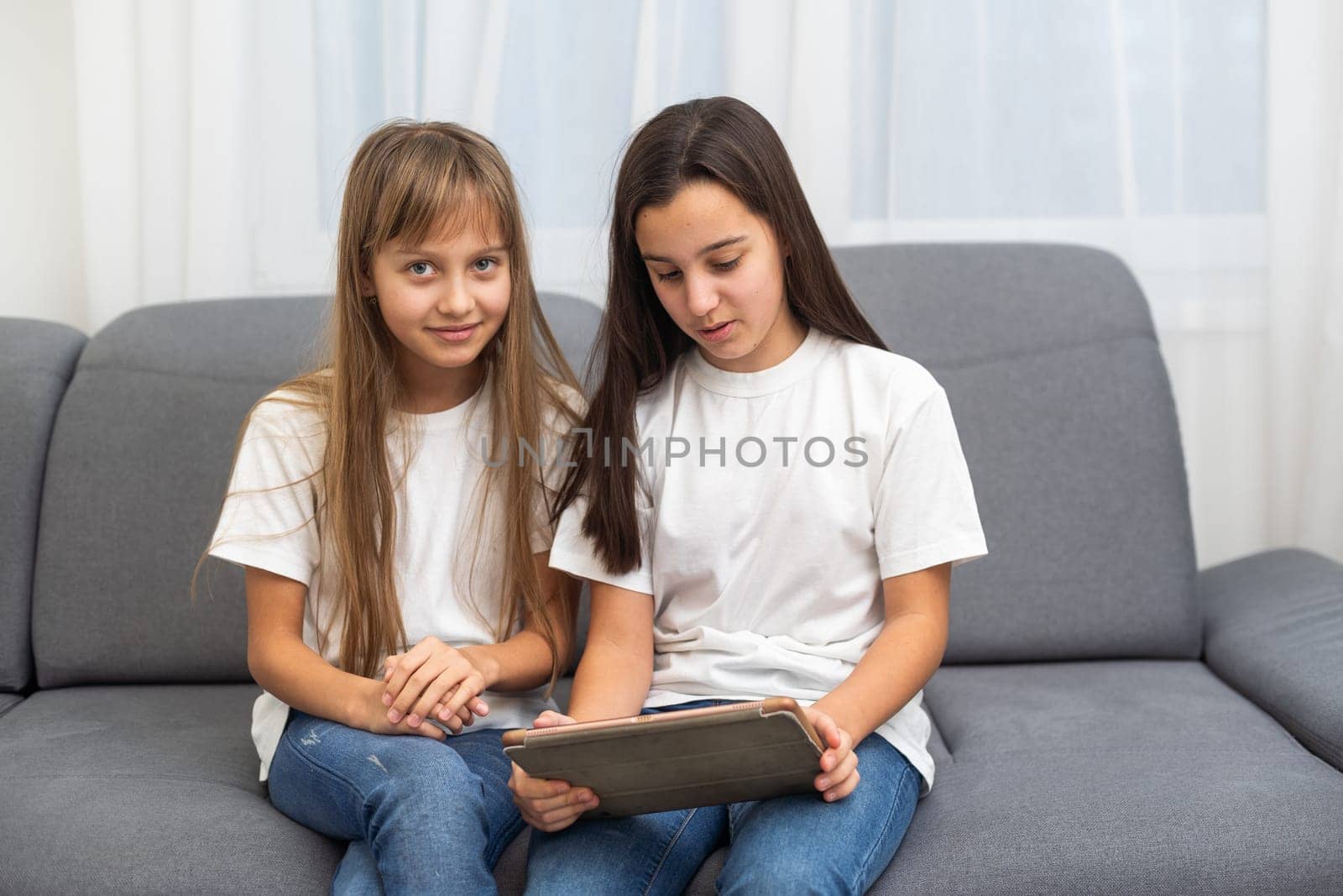 Cute little girl and older sister playing together smiling and having bonding time using a laptop on couch at home. Happy family Siblings relationship and digital technology lifestyle concept. by Andelov13