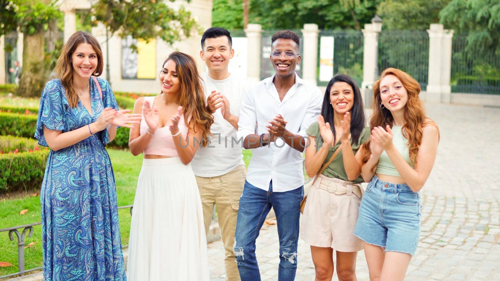 Group of multiethnic friends applauding while looking at the camera outdoors