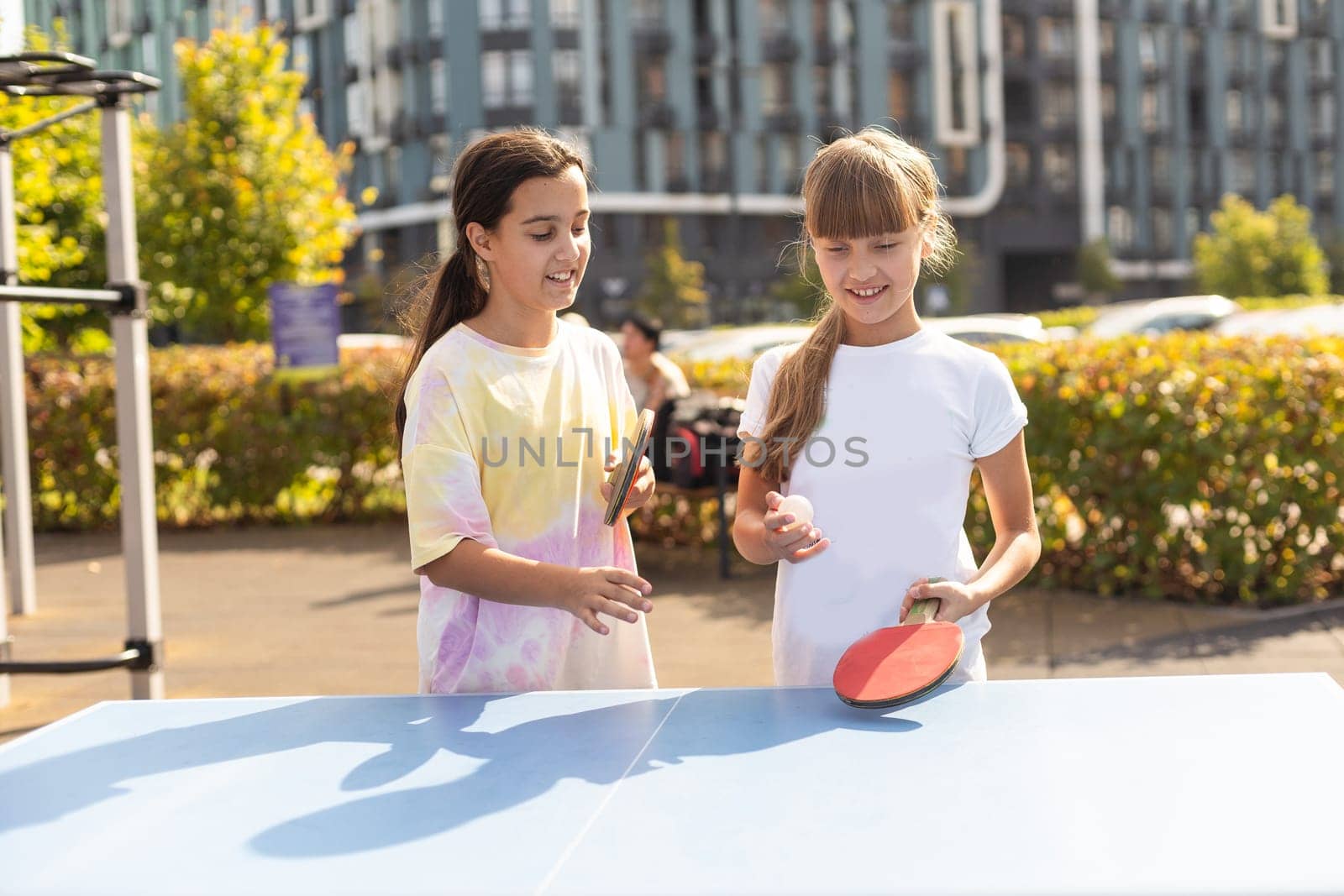 Young teenager girl playing ping pong. She holds a ball and a racket in her hands. Playing table tennis outdoors in the yard. High quality photo