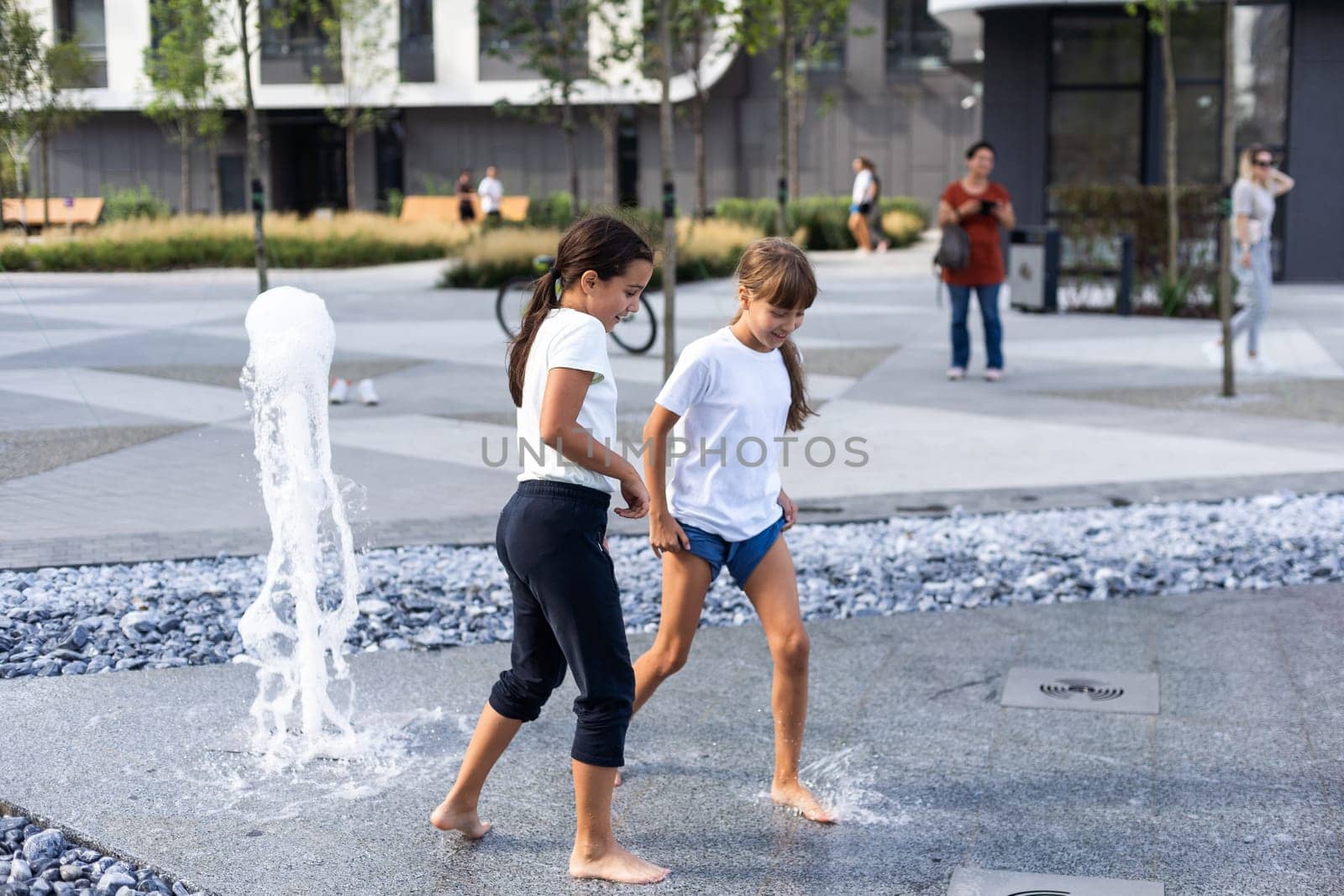 Cheerful young teen girl in city fountain, girl in wet clothes is having fun and enjoying the cool summer water, background city architecture. High quality photo