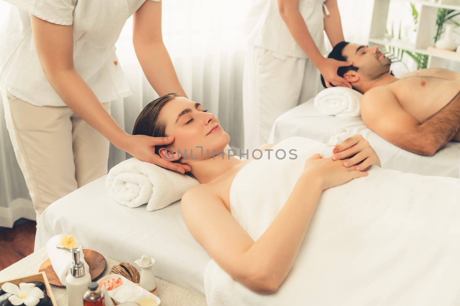 Caucasian couple enjoying relaxing anti-stress head massage and pampering facial beauty skin recreation leisure in dayspa modern light ambient at luxury resort or hotel spa salon. Quiescent