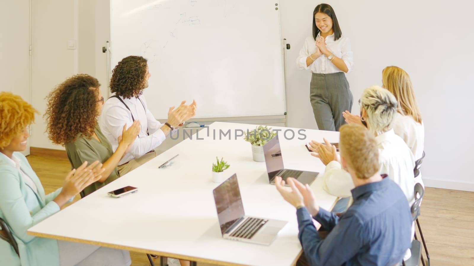Colleagues applauding a chinese woman after a speech in a meeting room