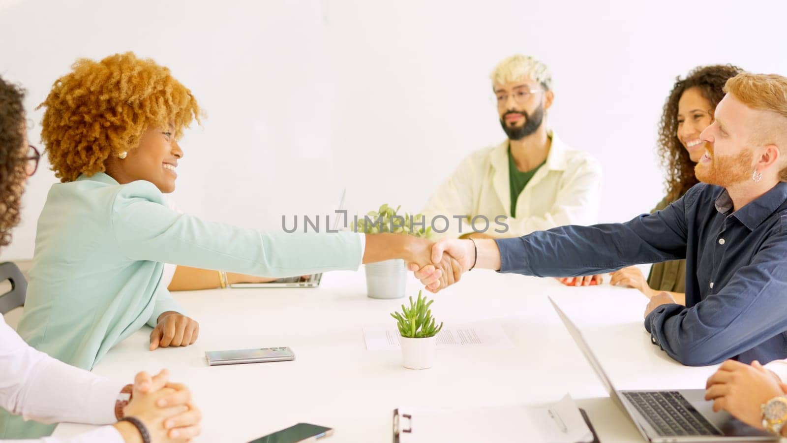 Business people handshaking sitting on a table with multi-ethnic coworkers by ivanmoreno