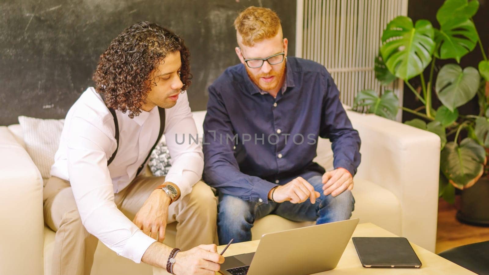 Two coworkers talking while using laptop sitting on a sofa