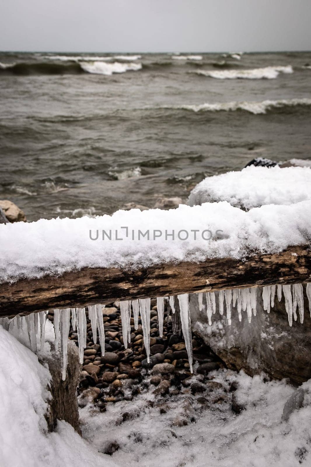 Icicles hanging from an old log on a rocky beach by Granchinho