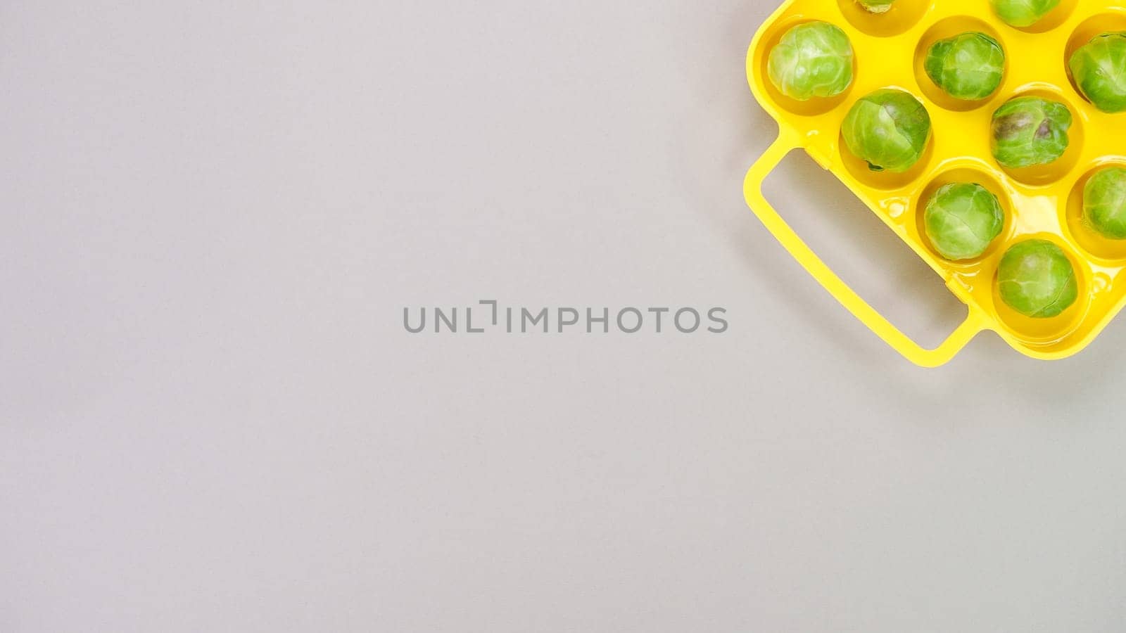 Raw organic Brussel sprouts in yellow container on grey background, top view. Flat lay, overhead, from above. Copy space. by JuliaDorian