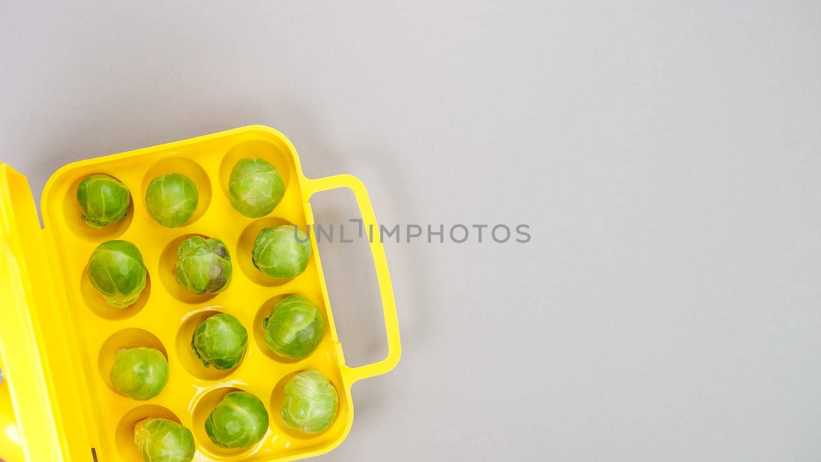 Raw organic Brussel sprouts in yellow container on grey background, top view. Flat lay, overhead, from above. Copy space. by JuliaDorian
