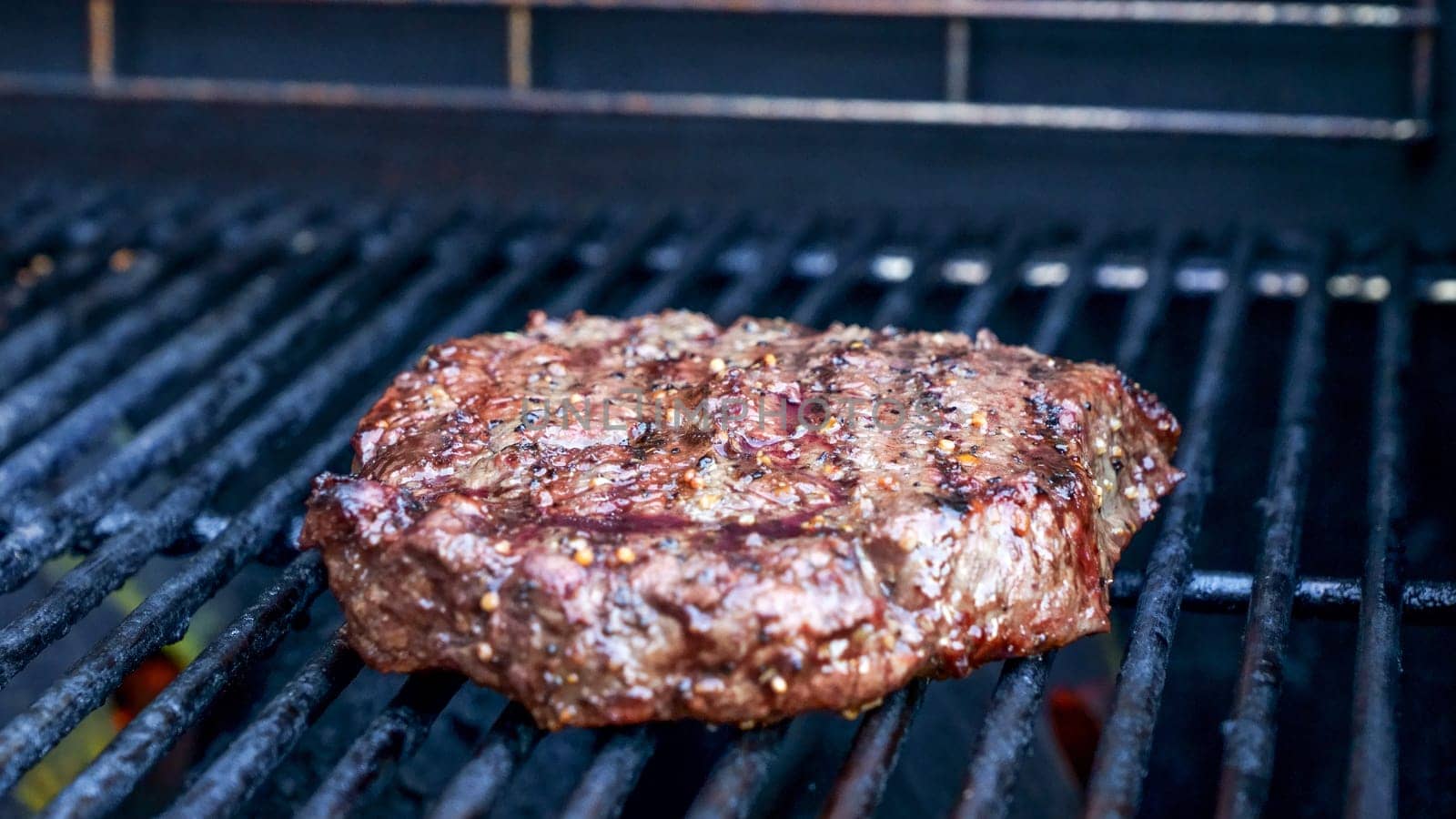 Grilled meat steak on stainless BBQ grill with flames on dark background. Food and cuisine concept. by JuliaDorian