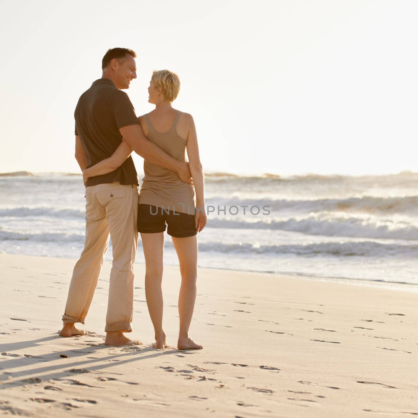 Love, beach and back of couple at sunset for bonding, relax together and relationship by ocean. Dating, travel and man and woman hug, embrace and smile on holiday, vacation and weekend in nature.