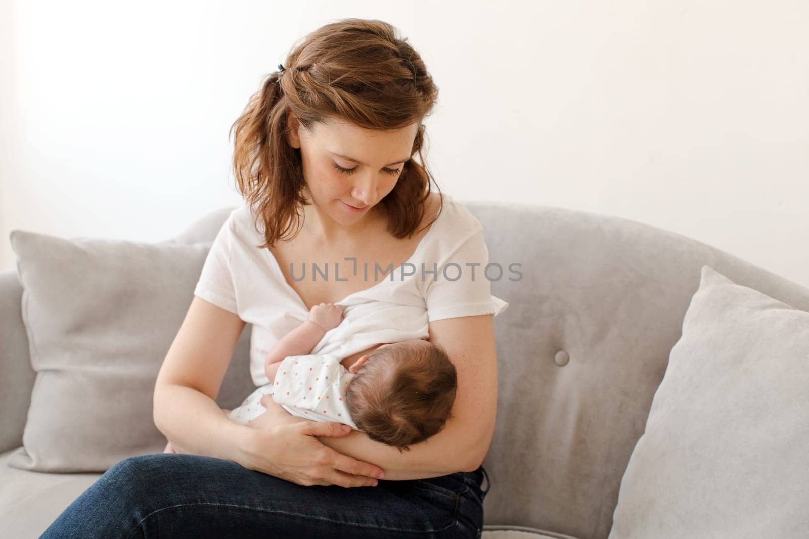 Happy mother breastfeeding baby sitting on sofa by Demkat