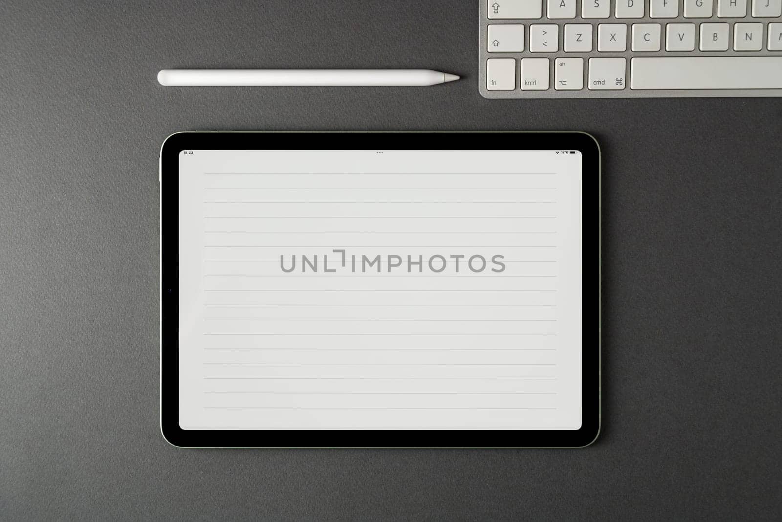 Tablet with lined notepaper on the screen and a keyboard and stylus pen on a dark gray table by Sonat