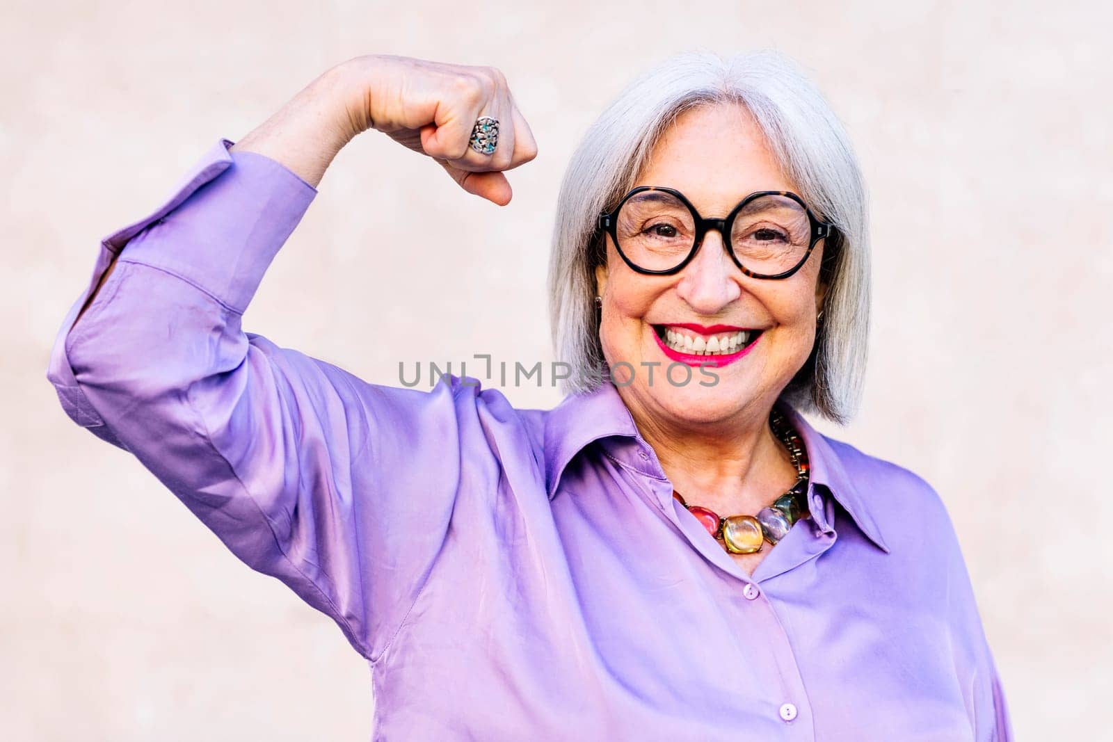 smiling senior woman looking at camera showing muscle with her arm, concept of strength and happiness of elderly people and active lifestyle
