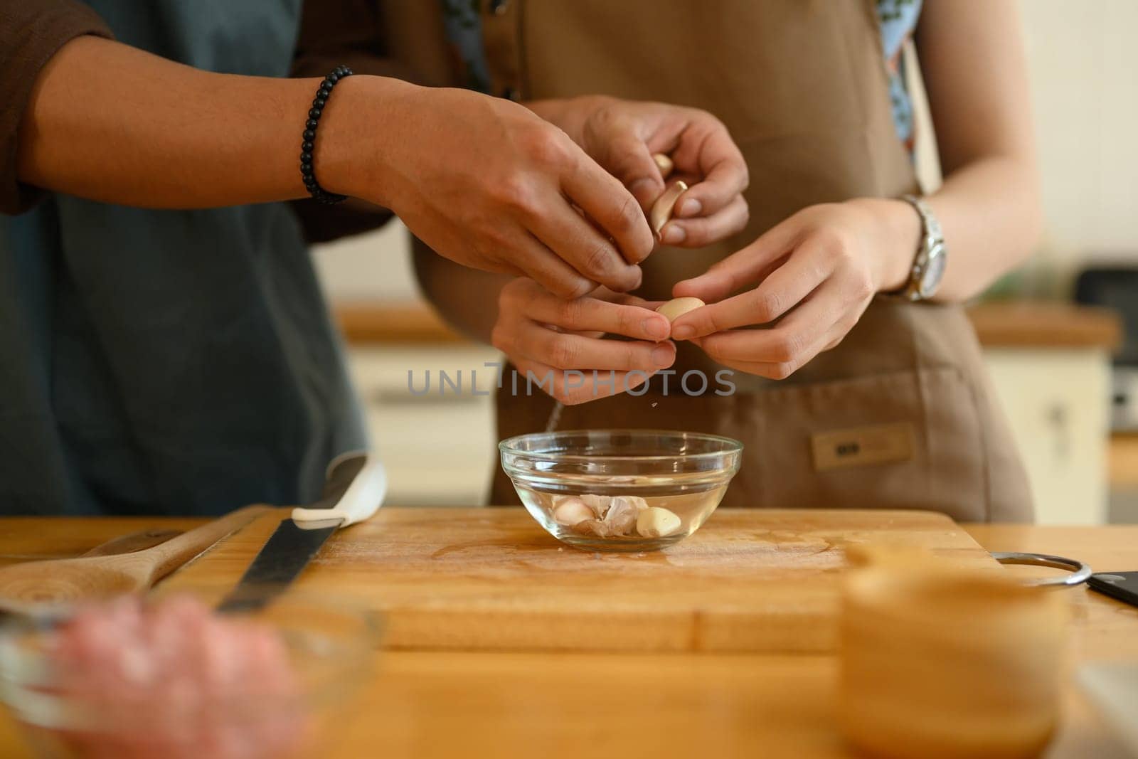 Hands of young couple peeling garlic on wooden chopping board. Healthy lifestyle concept.