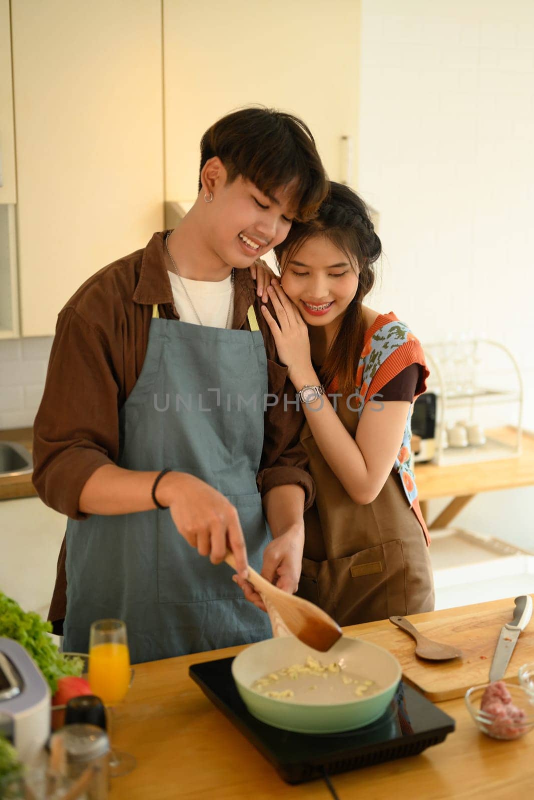 Portrait of affectionate young couple wearing aprons cooking together in the kitchen at home by prathanchorruangsak