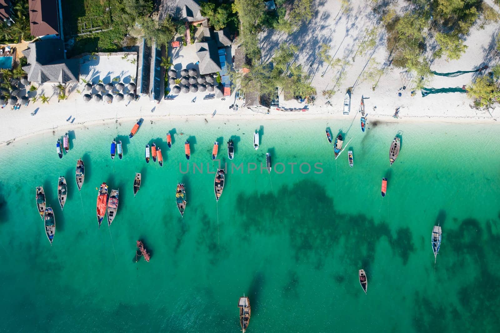 Aerial view of the fishing boats and umbrellas on tropical sea coast with sandy beach.Summer travel in Zanzibar, Africa.Top view of boats and clear green water.