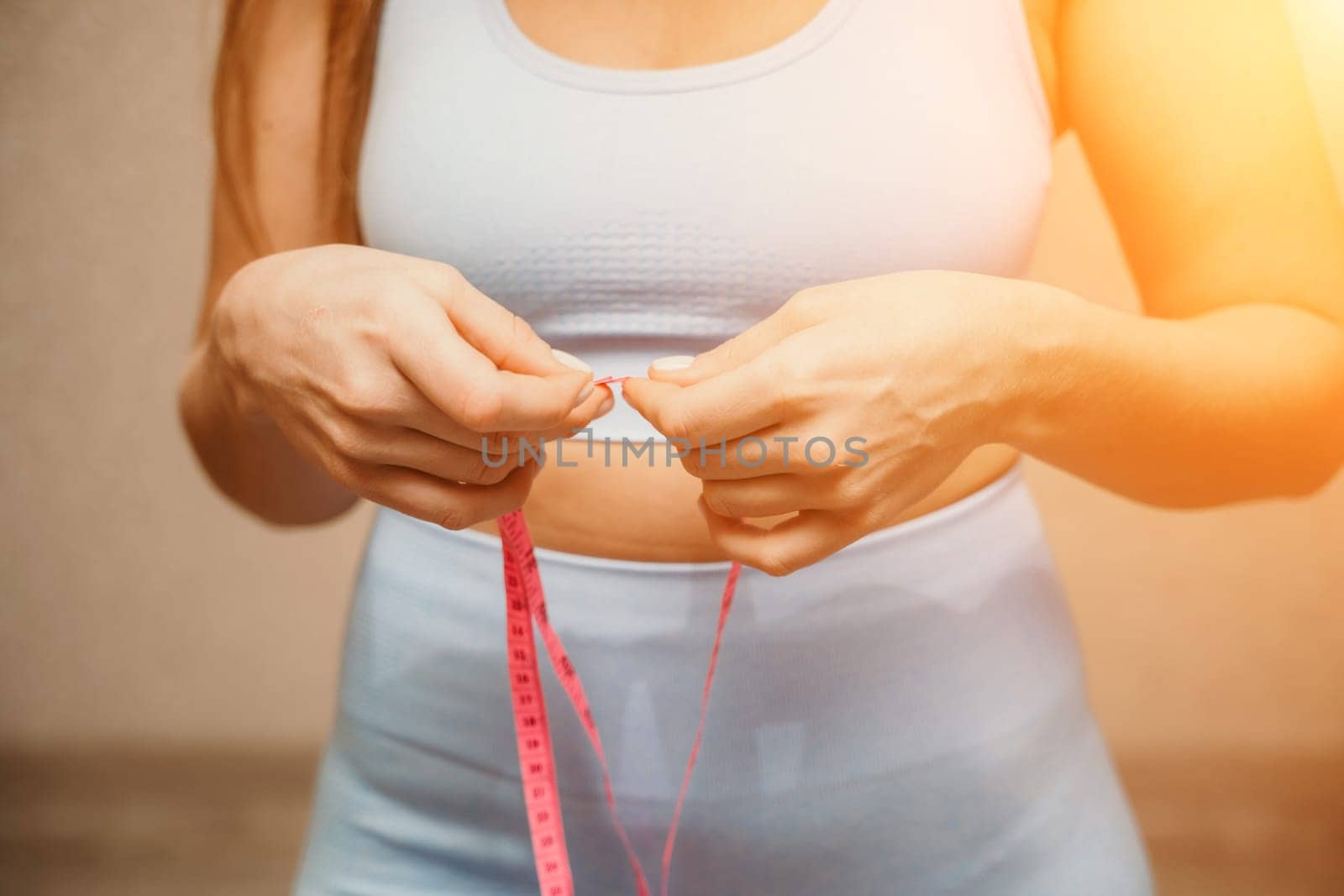 Cropped view of slim woman measuring waist with tape measure at home, close up. European woman checking the result of diet for weight loss or liposuction indoors by Matiunina