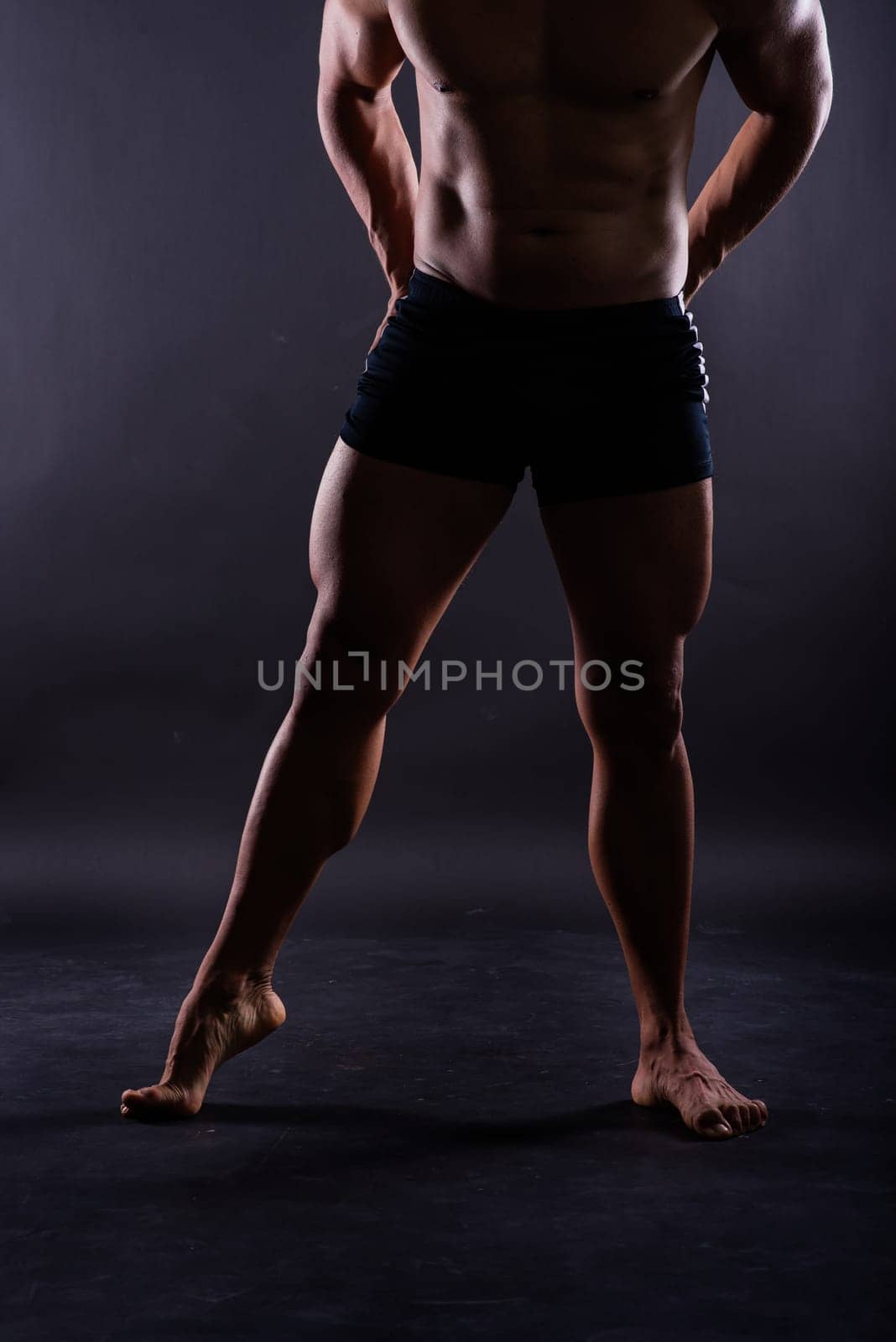 Muscular male legs, man in a studio, dark background