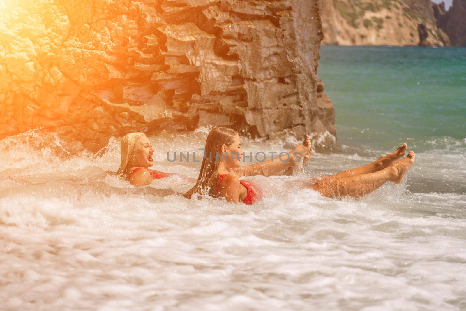 Women ocean play. Seaside, beach daytime, enjoying beach fun. Two women in red swimsuits enjoying themselves in the ocean waves. by Matiunina