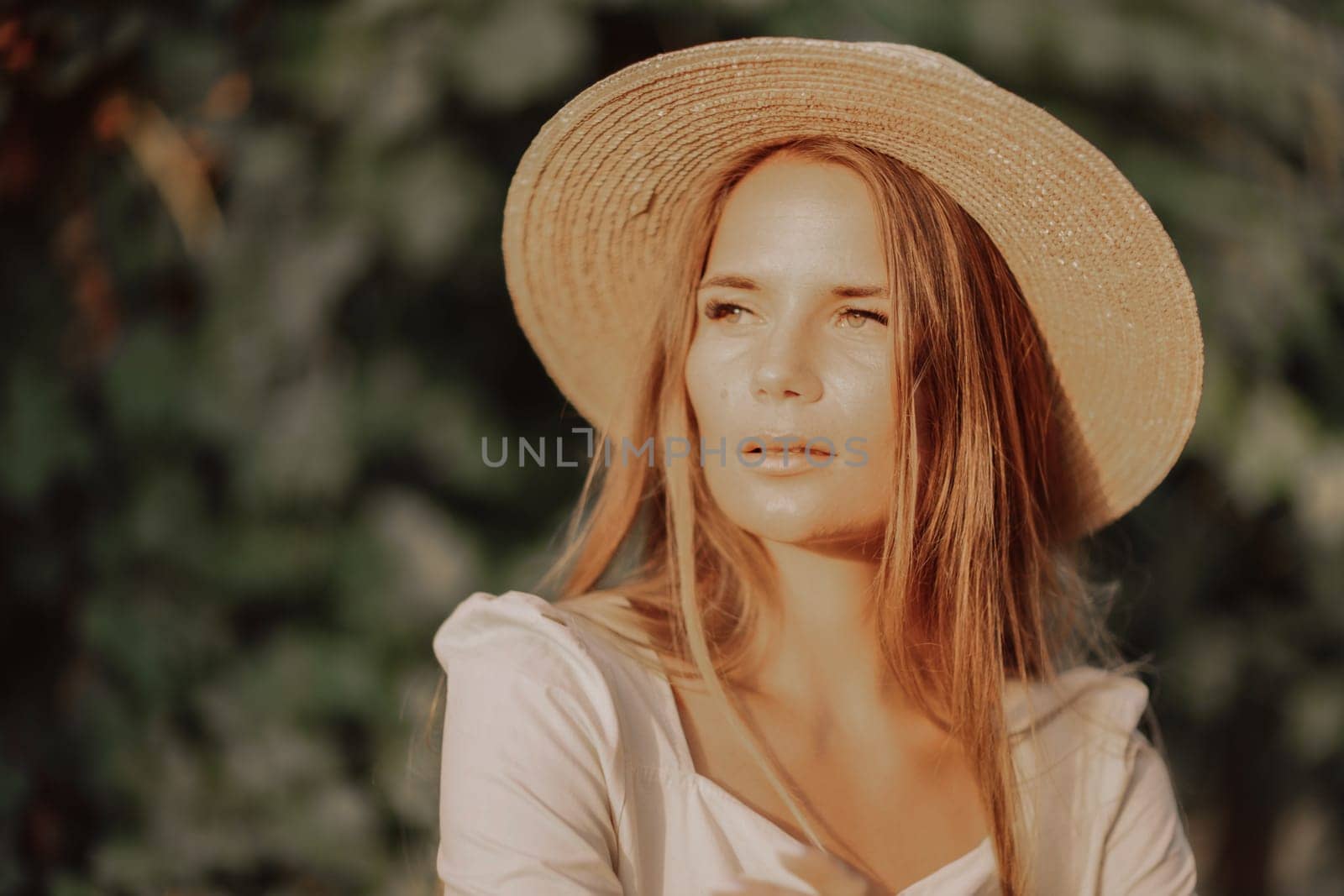 Woman with straw hat stands in front of vineyard. She is wearing a light dress and posing for a photo. Travel concept to different countries.