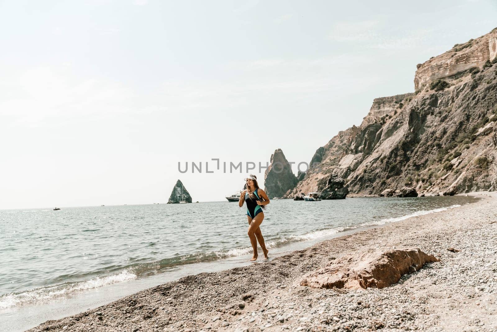 Woman beach vacation photo. A happy tourist in a blue bikini enjoying the scenic view of the sea and volcanic mountains while taking pictures to capture the memories of her travel adventure