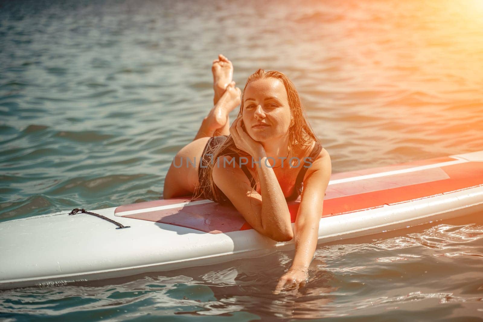Woman sup sea. Sports girl on a surfboard in the sea on a sunny summer day. In a black bathing suit, he sits on a sapa in the sea. Rest on the sea