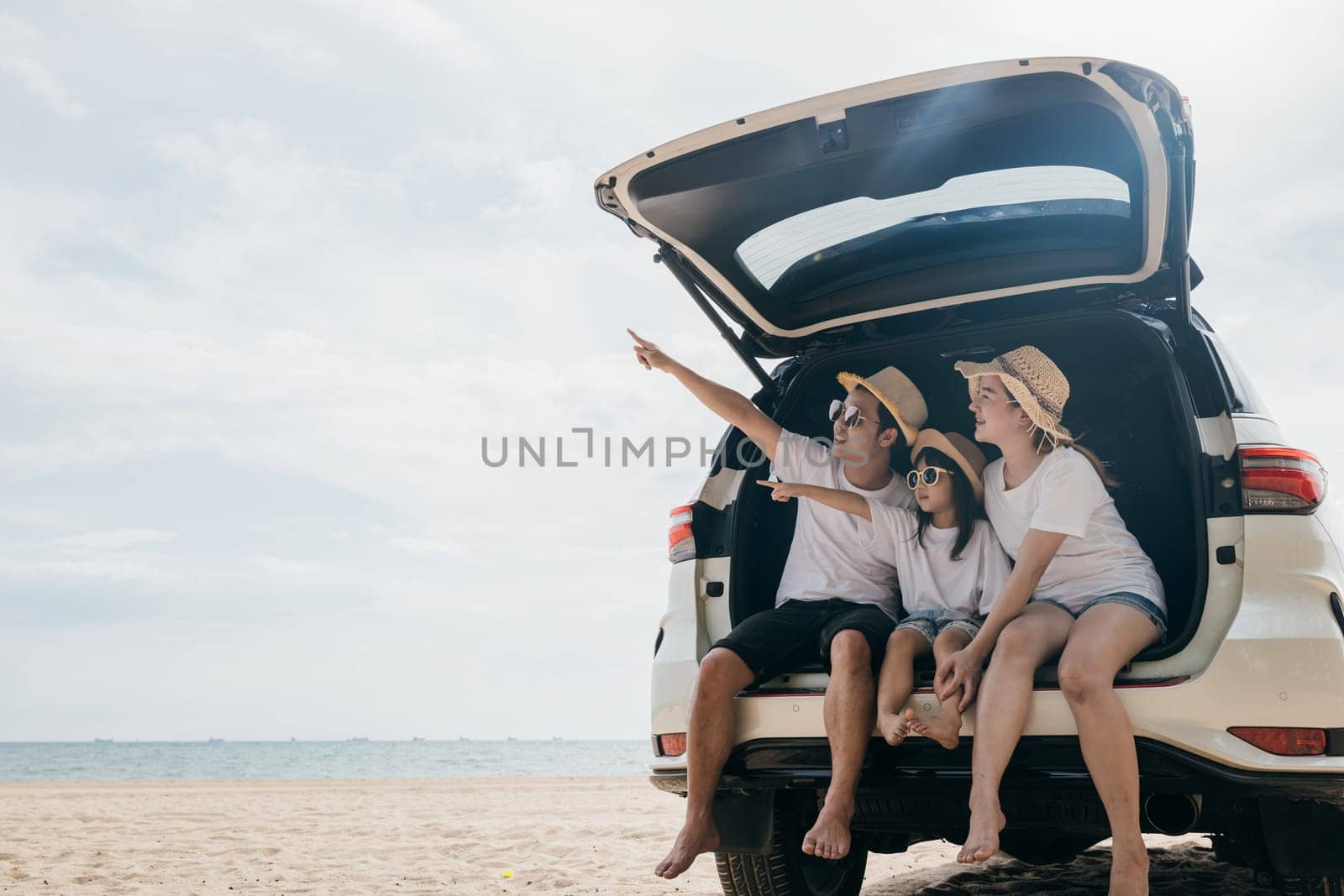 Family Day. Father, Mother and daughter enjoying road trip sitting on back car and point finger out blue sky, Happy people having fun in summer vacation on beach, Family travel in holiday at sea beach