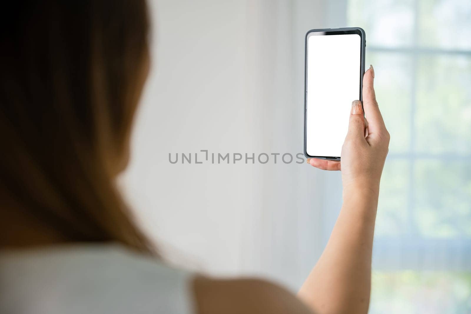 Happy Asian young woman checking social media holding smartphone at home while relaxing on sofa living room, Smile beautiful female sitting on couch using mobile phone to shopping online