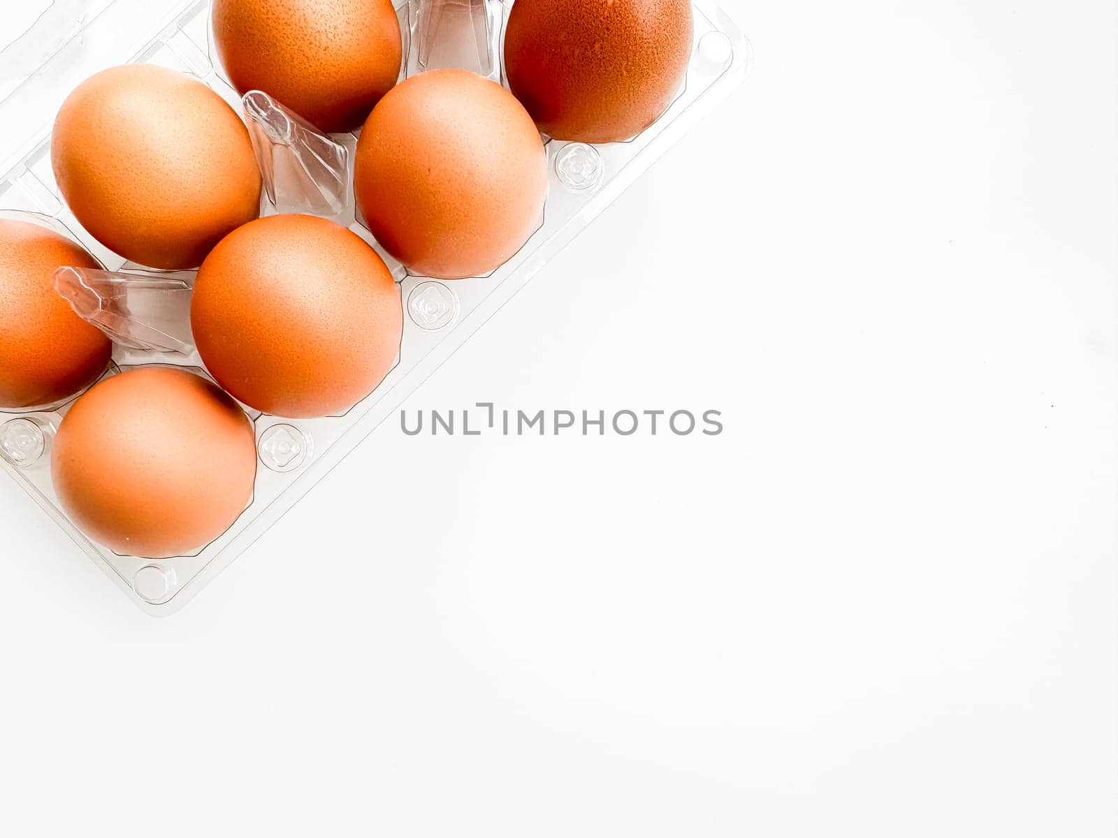 Brown eggs in transparent plastic carton on white background, top corner view. Concept of organic produce, breakfast essentials, and healthy eating with copy space. by Lunnica