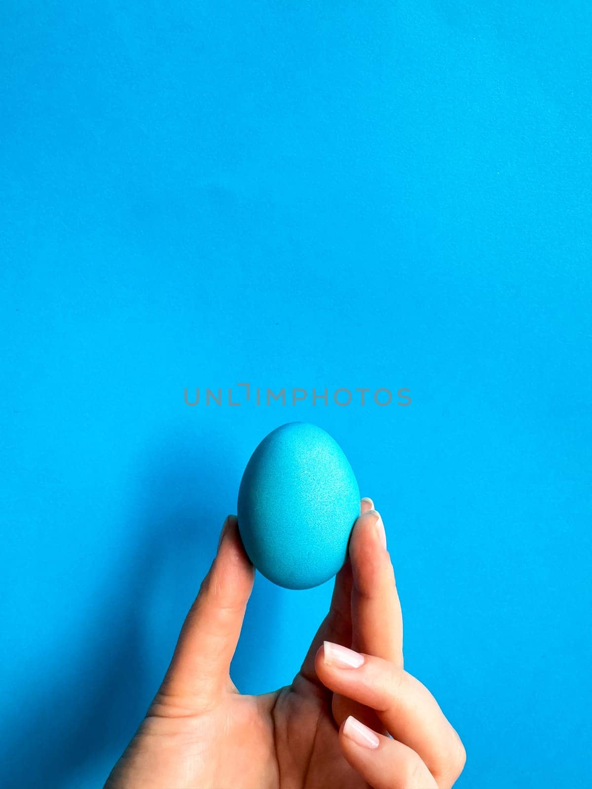 Hand balancing blue egg on a fingertip against solid blue background, minimalist concept for balance, Easter, and simplicity with space for text. High quality photo