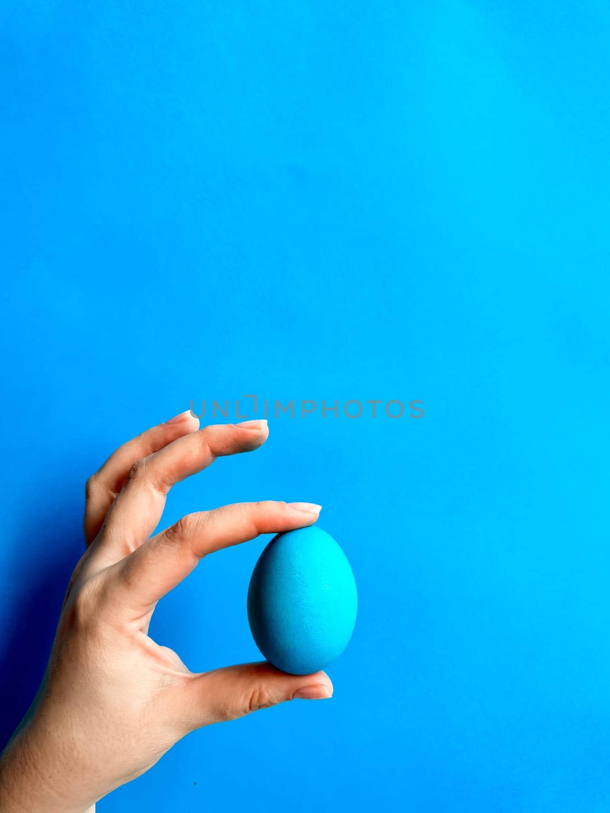 Hand balancing blue egg on a fingertip against solid blue background, minimalist concept for balance, Easter, and simplicity with space for text. High quality photo