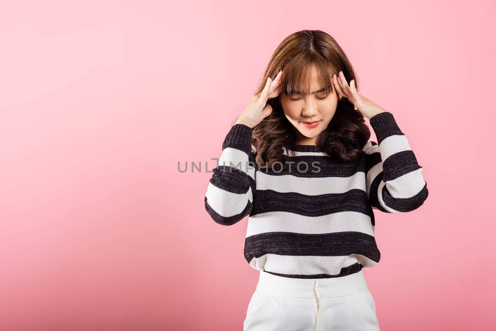 Portrait of beautiful Asian young woman sad tired strain face holding hold head by hands, stress female person unhappy closed eyes problem she headache, studio shot isolated on pink background