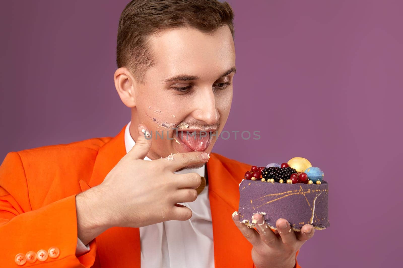 birthday man in orange jacket eating yummy cake on purple background