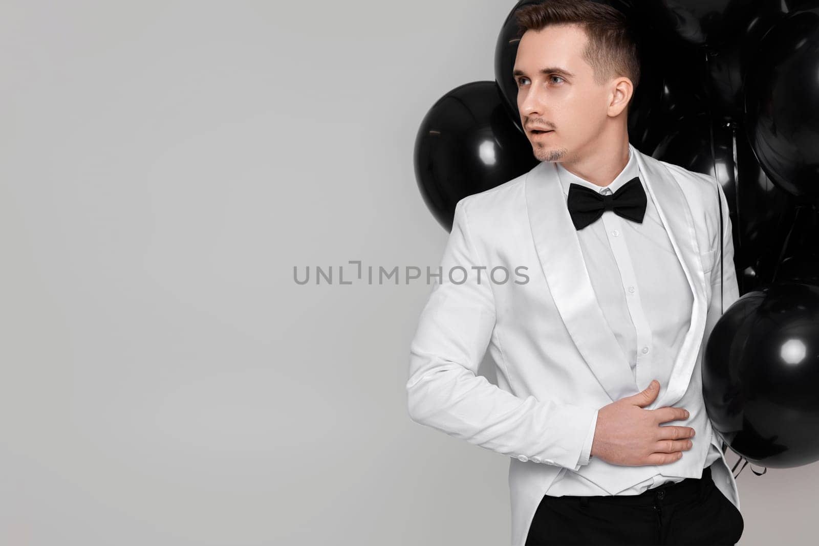 handsome man in white suit tuxedo with black air balloons. copy space