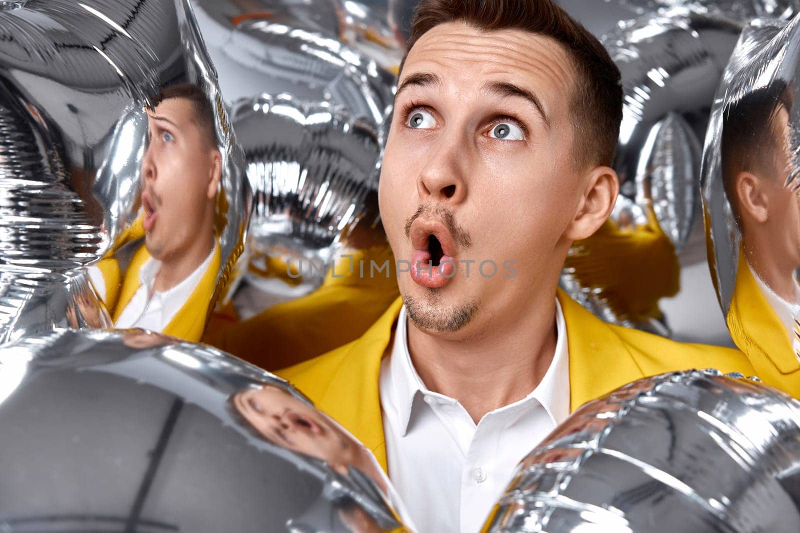 portrait of surprised man in yellow jacket with a lot of silver air balloons. birthday party