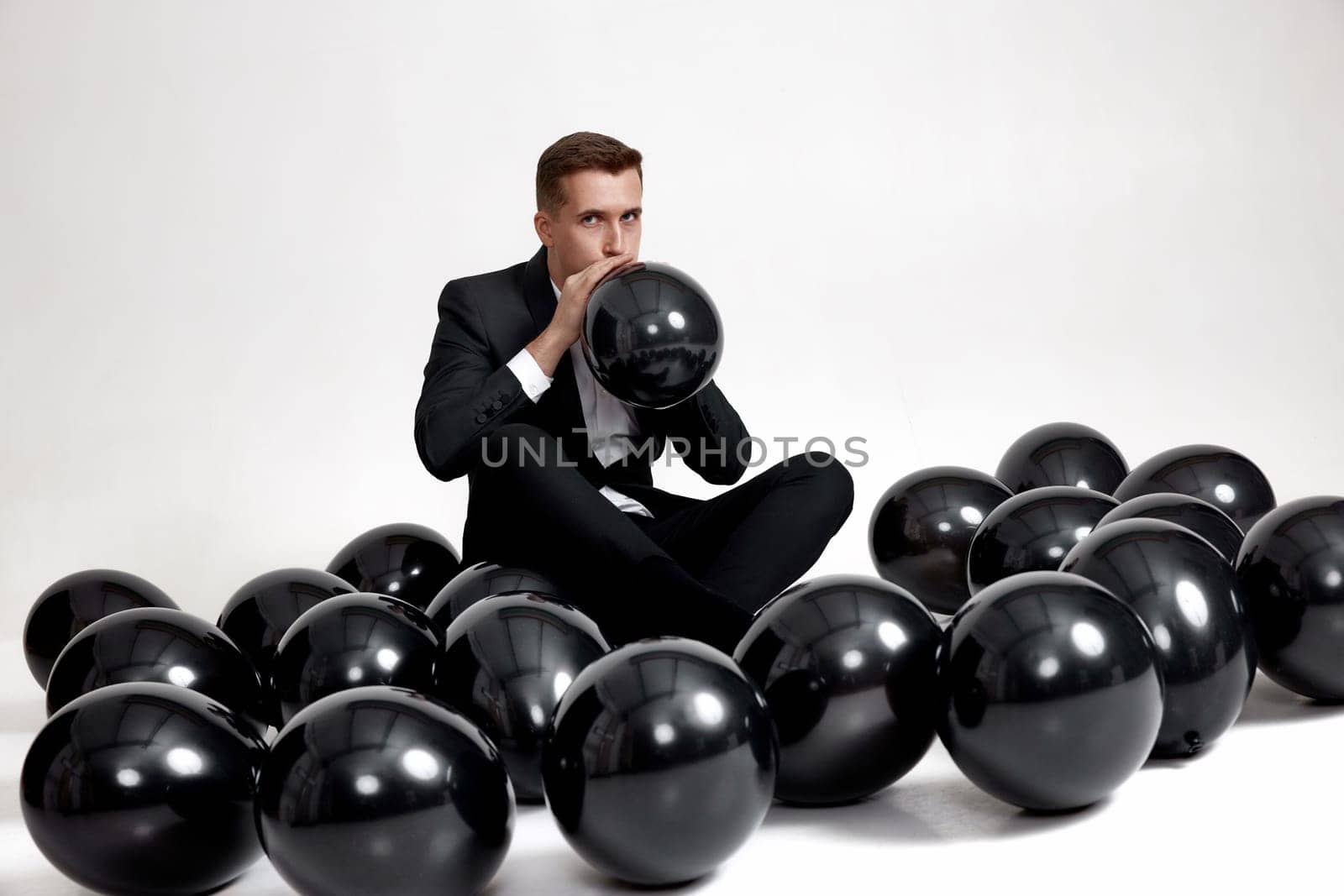 handsome man in black jacket blowing black air balloon on white studio background. new year party