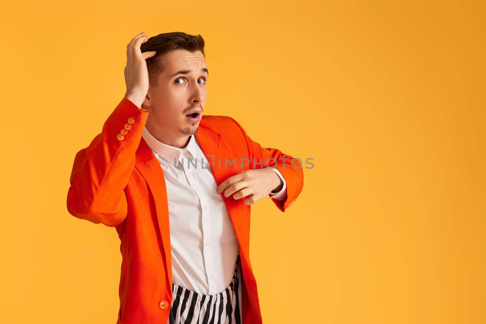Cheerful funny young man in orange jacket and striped pants on yellow background.