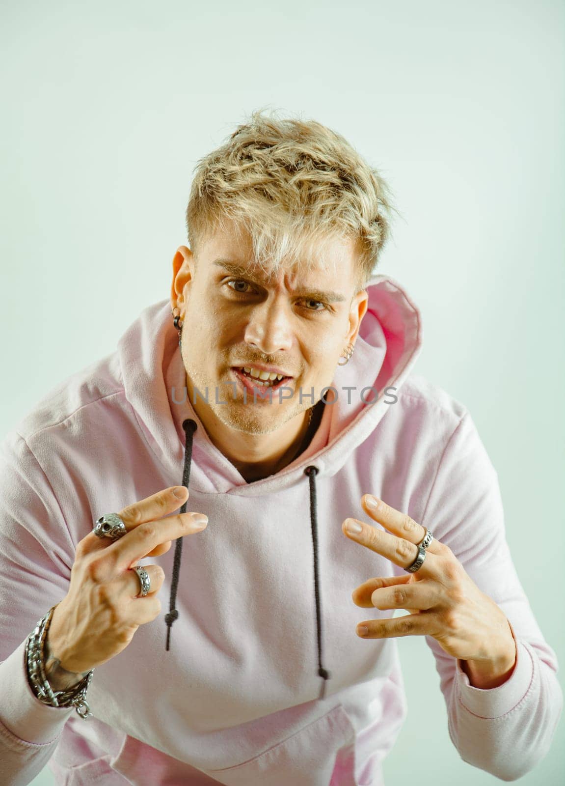 A man wearing a pink hoodie is standing with his hands outstretched in this image. He appears to be in a public area and is the sole focus of the photo.