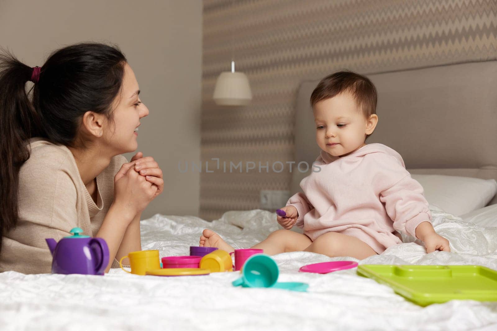 smiling mother and little child daughter playing tea party and spending time together in bedroom, family having fun