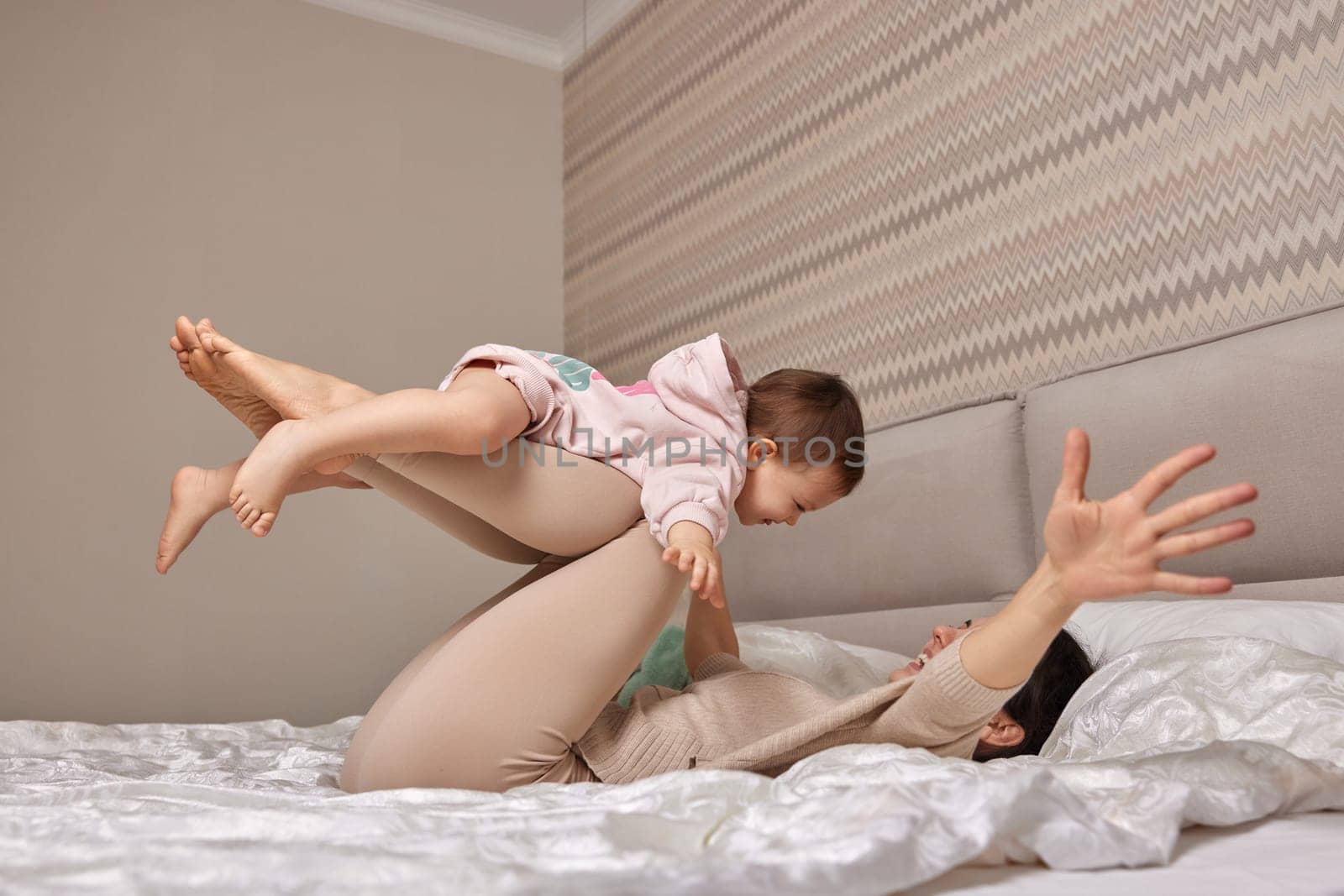 Happy Caucasian mother lifting in air cute little child daughter in bedroom