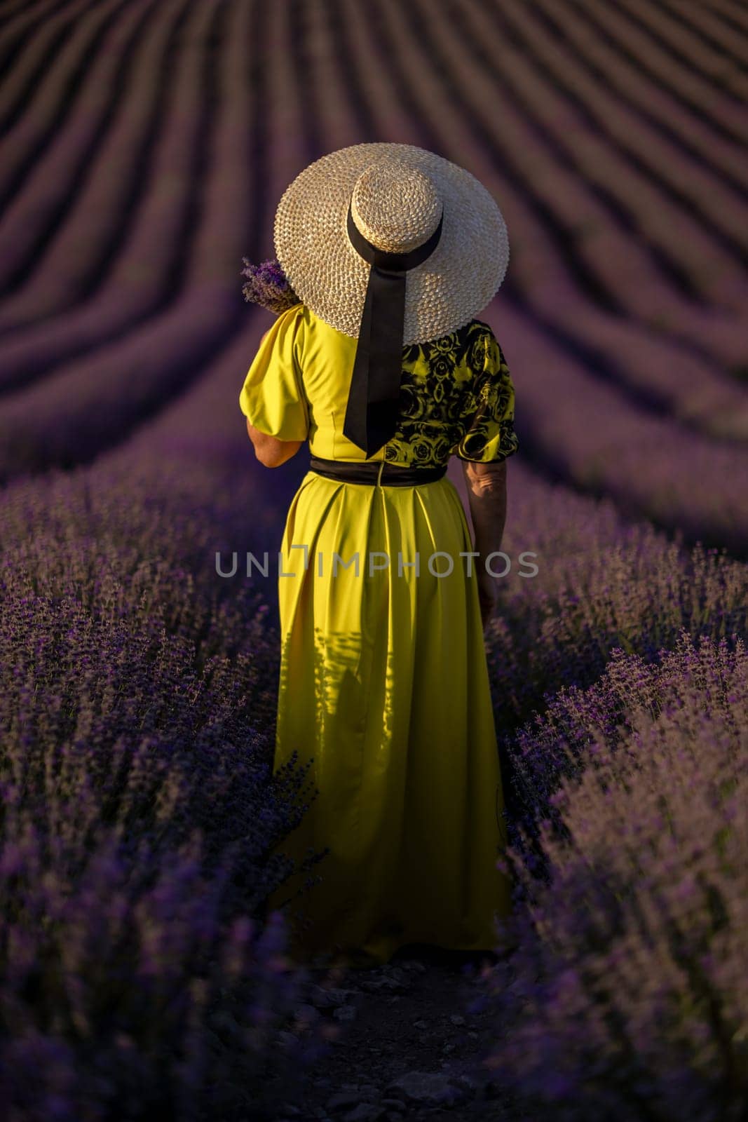 Back view woman lavender sunset. Happy woman in yellow dress holds lavender bouquet. Aromatherapy concept, lavender oil, photo session in lavender by Matiunina