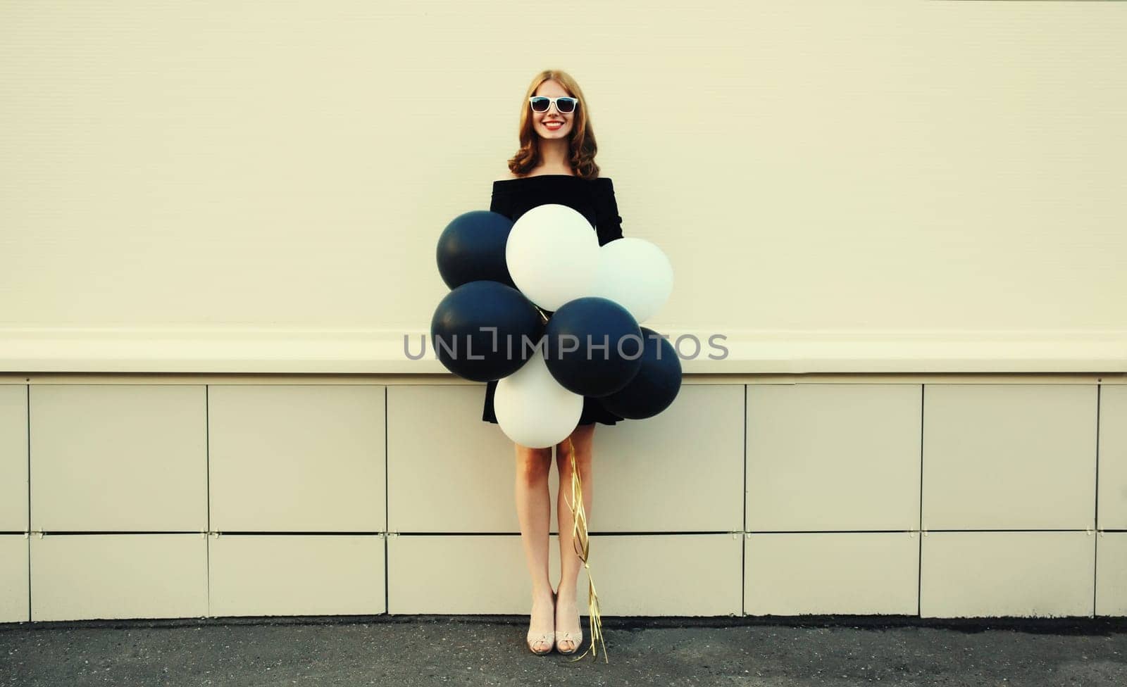 Beautiful happy young woman with bunch of black and white balloons in summer dress on city street by Rohappy