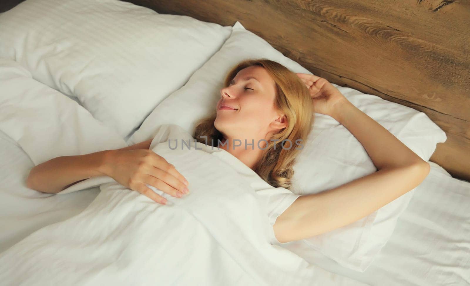 Young woman sleeping lying in bed on white soft comfortable pillow in bedroom at home by Rohappy