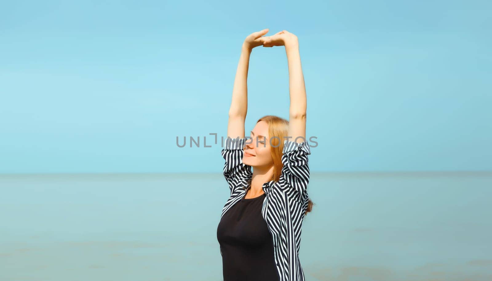 Summer vacation, happy relaxing healthy young woman meditates and enjoying fresh air on the beach on sea coast and blue sky background